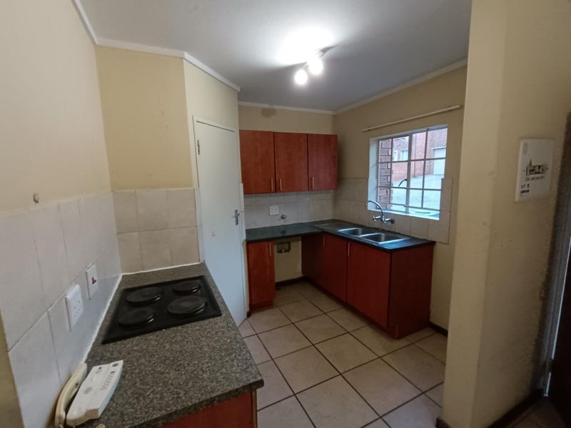 A functional kitchen featuring built-in cabinetry, laminate countertops, an electric hob, and a double basin sink with tiled flooring and splashbacks.
