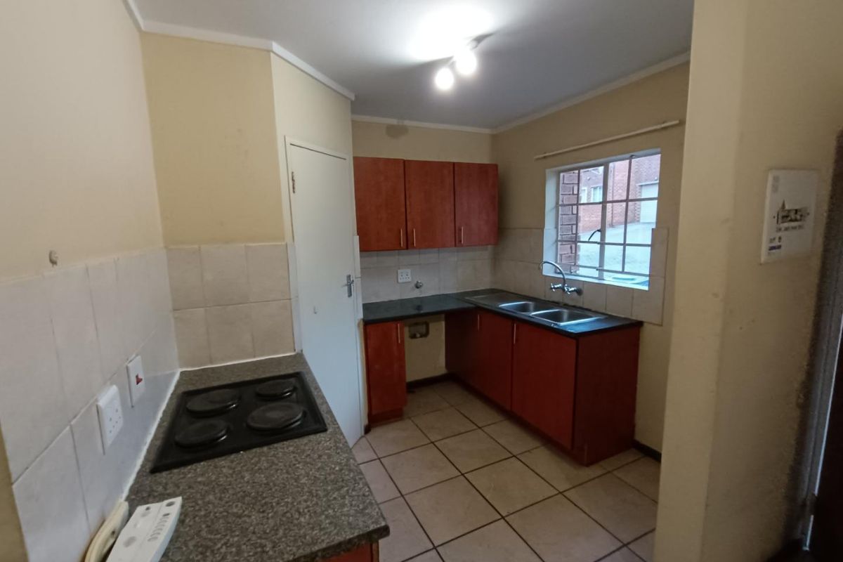 A functional kitchen featuring built-in cabinetry, laminate countertops, an electric hob, and a double basin sink with tiled flooring and splashbacks.