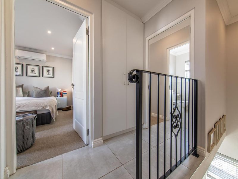 A bright hallway featuring tiled flooring, built-in storage cupboards, and a decorative wrought iron balustrade, providing access to adjacent bedrooms and bathrooms.