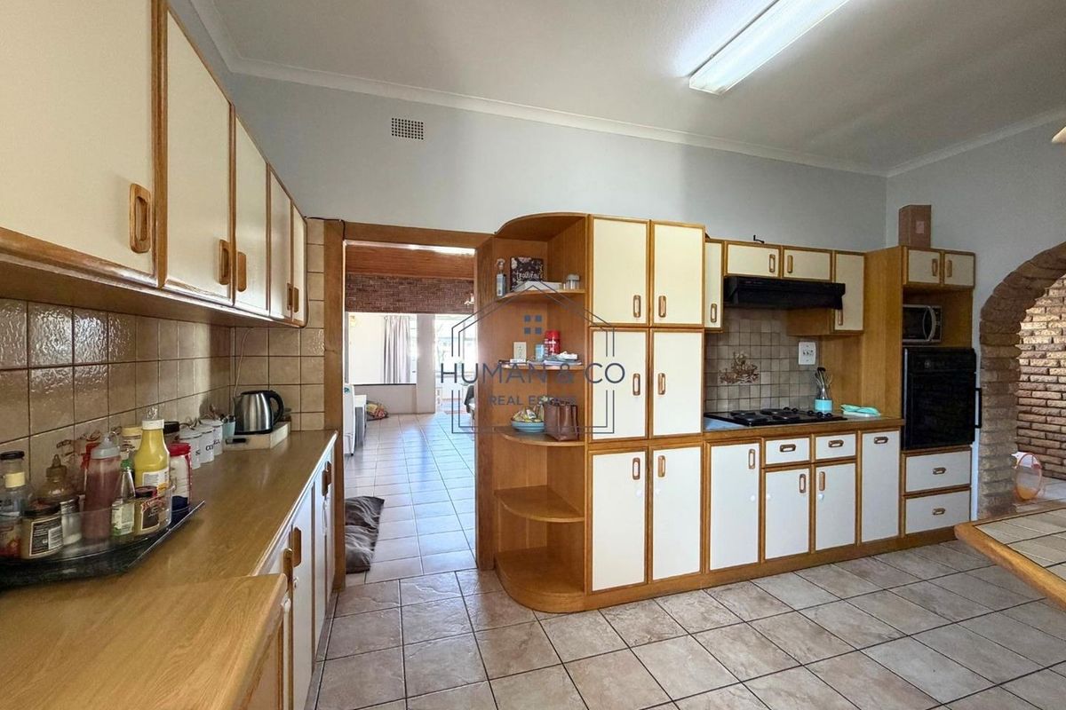 A functional kitchen featuring traditional cabinetry, tiled flooring, built-in oven, and hob, with an open flow into the adjacent living area.