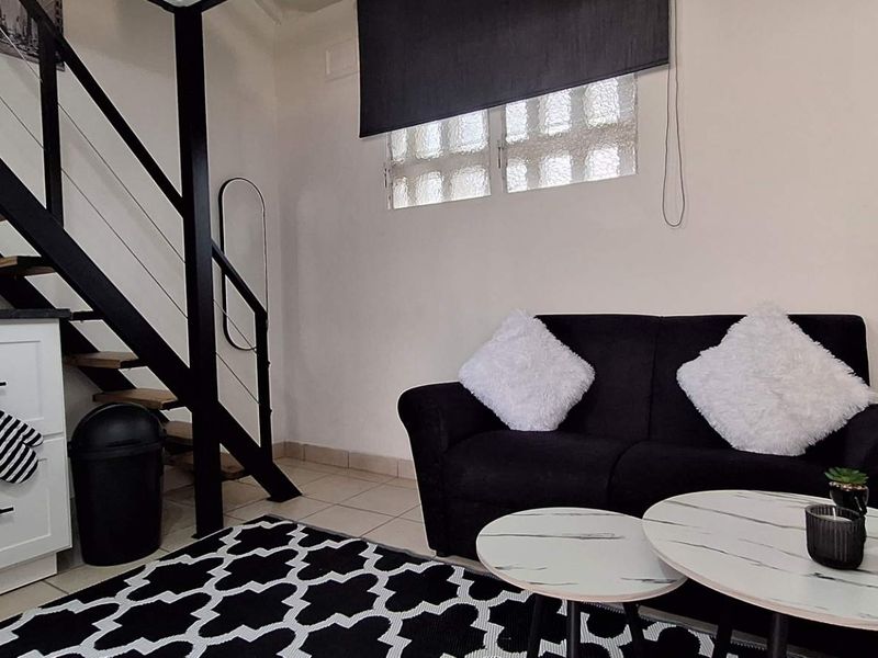 Open plan living area featuring a modern staircase with metal handrails, tiled flooring, and a glass block window providing natural light.