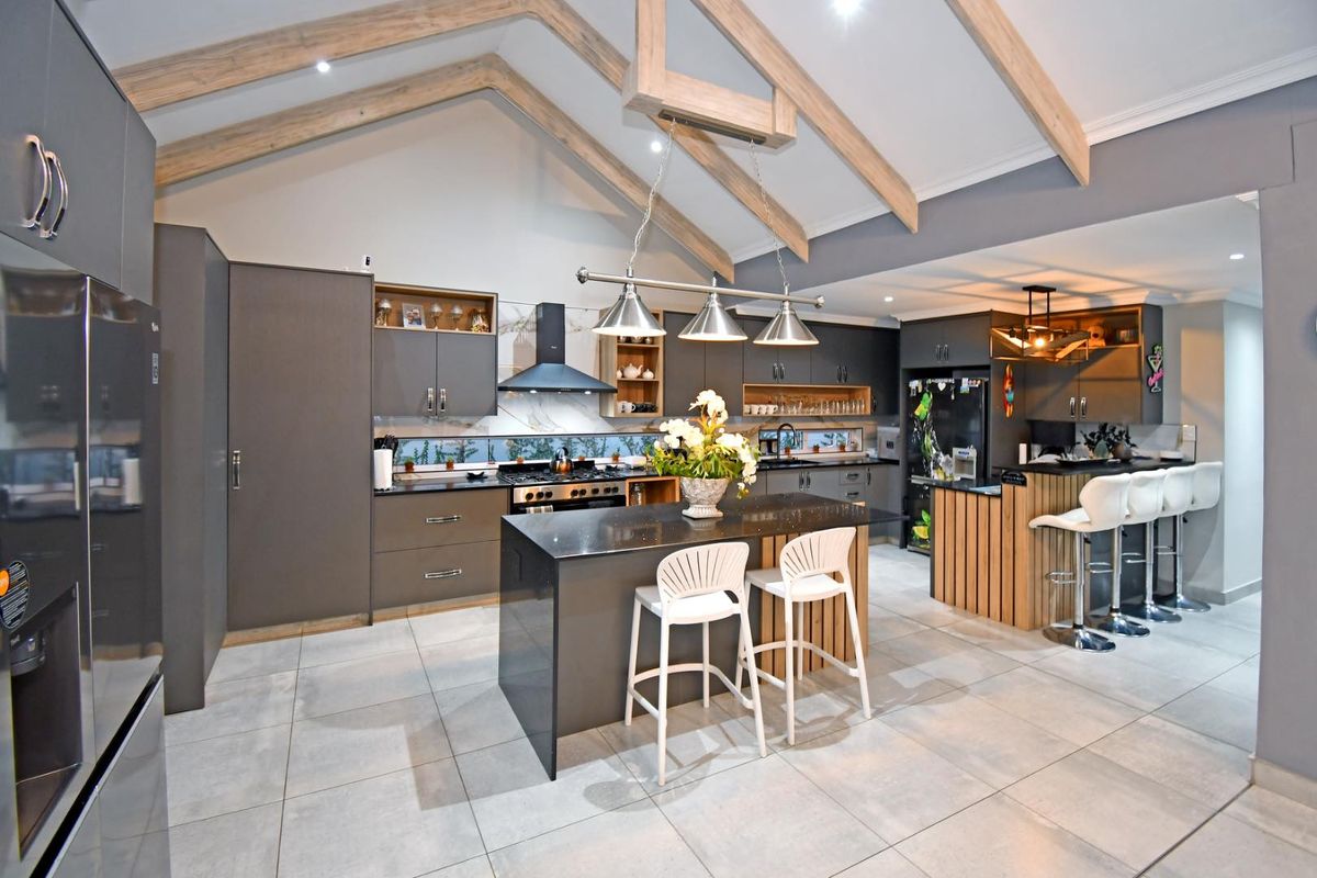 Modern open-plan kitchen featuring vaulted ceilings with exposed timber beams, a central island with stone countertops, and high-end cabinetry.