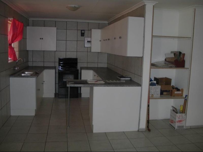 A functional kitchen featuring white cabinetry, laminate countertops, a stainless steel sink, and tiled finishes throughout. The space offers practical storage and workspace.
