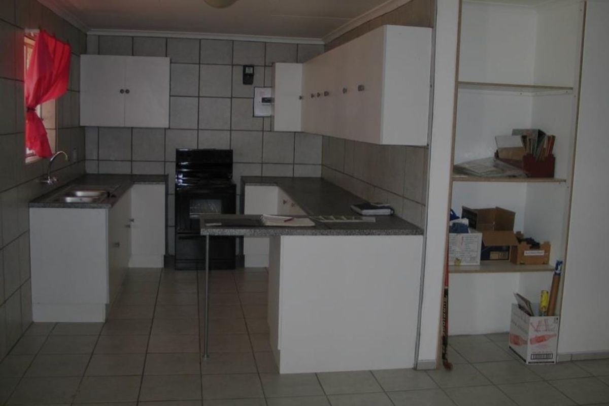 A functional kitchen featuring white cabinetry, laminate countertops, a stainless steel sink, and tiled finishes throughout. The space offers practical storage and workspace.