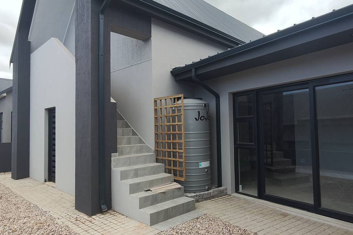 Modern exterior rear view featuring a paved courtyard, external staircase, and a rainwater storage tank integrated into the contemporary building design.