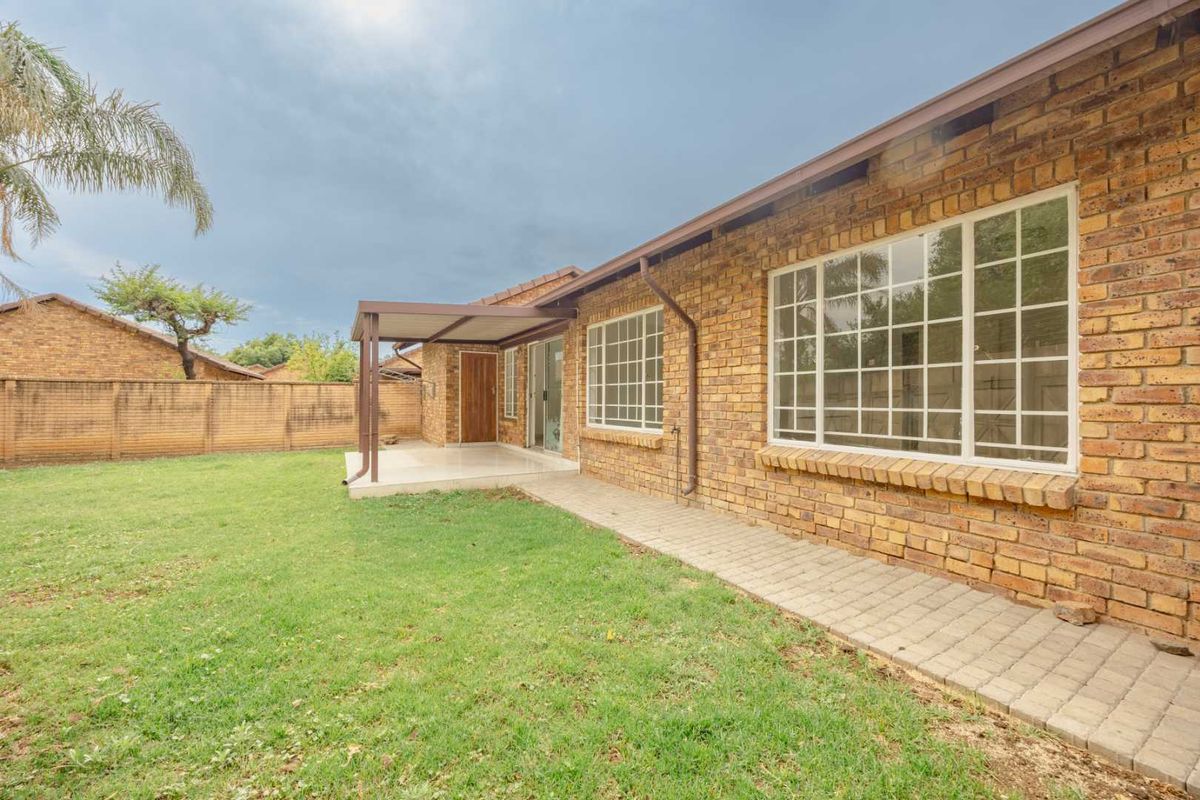 Rear view of the townhouse featuring a face brick facade, a covered patio area, a paved walkway, and a private garden with a boundary wall.