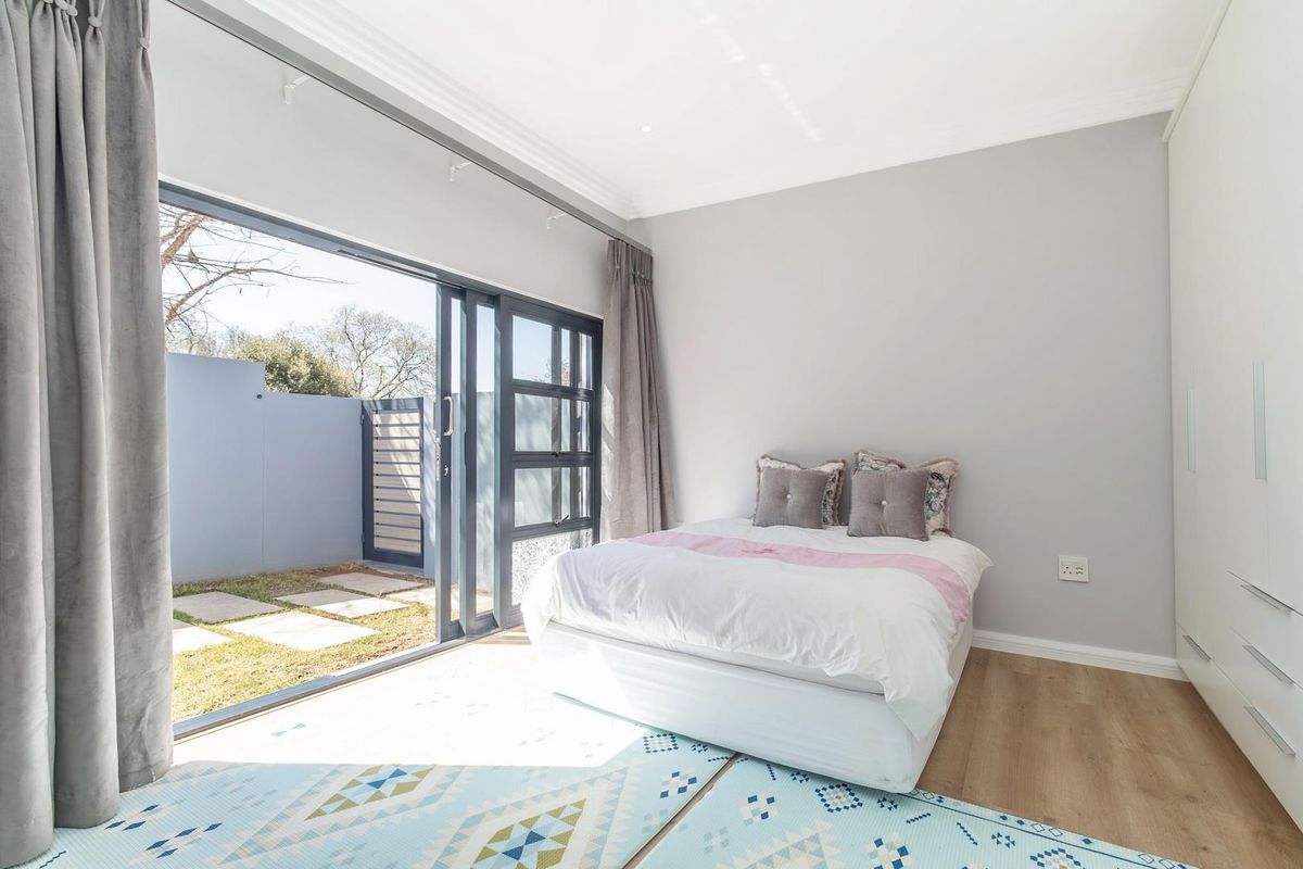 A bright bedroom featuring modern laminate flooring, built-in cupboards, and large sliding glass doors that open directly onto a private paved garden area.