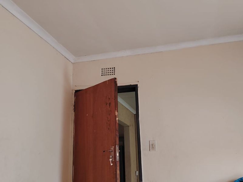 A simple bedroom interior featuring a timber door, ventilation grille, and coving, requiring cosmetic updates to improve the overall finish.