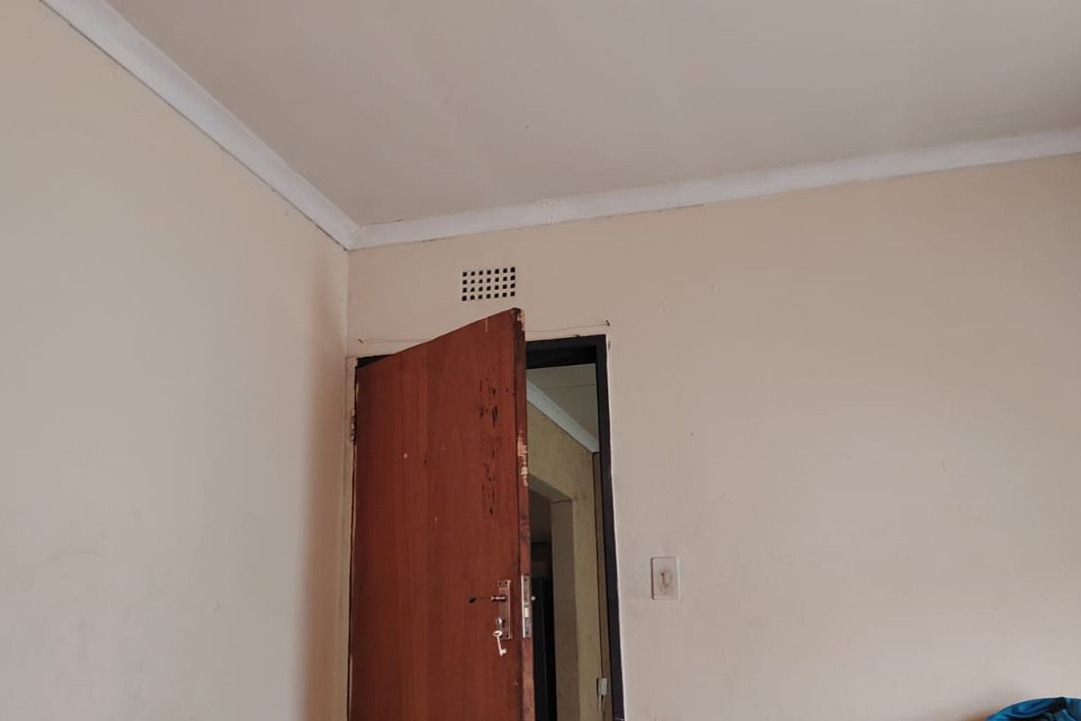 A simple bedroom interior featuring a timber door, ventilation grille, and coving, requiring cosmetic updates to improve the overall finish.