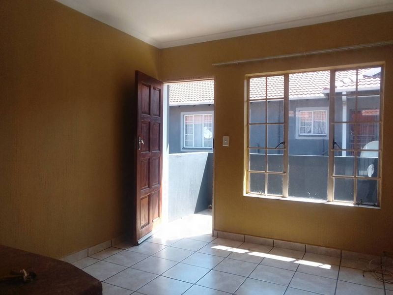 An empty living area featuring tiled flooring, a timber door leading to an exterior space, and large grid-pattern windows allowing natural light.