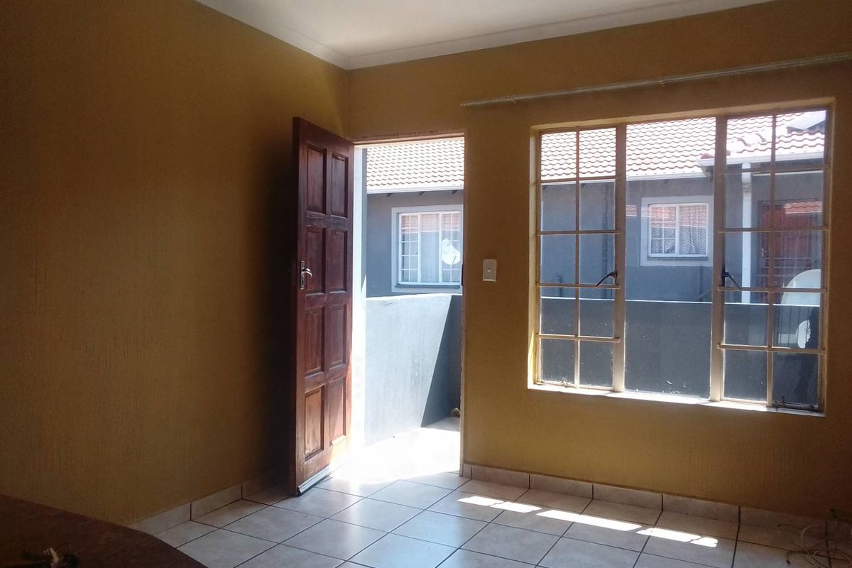 An empty living area featuring tiled flooring, a timber door leading to an exterior space, and large grid-pattern windows allowing natural light.