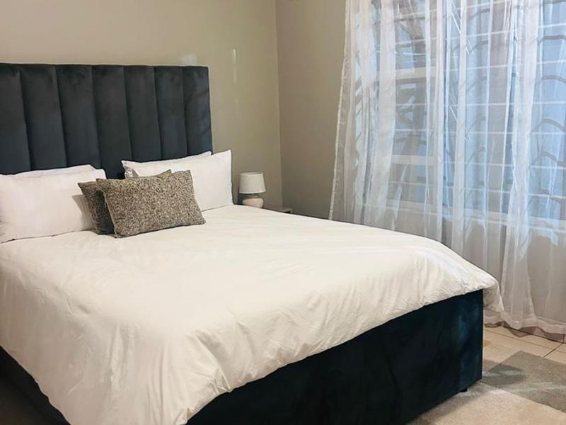 A well-maintained bedroom featuring tiled flooring, an integrated air conditioning unit, and security bars on the window.