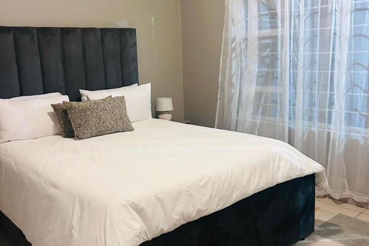 A well-maintained bedroom featuring tiled flooring, an integrated air conditioning unit, and security bars on the window.