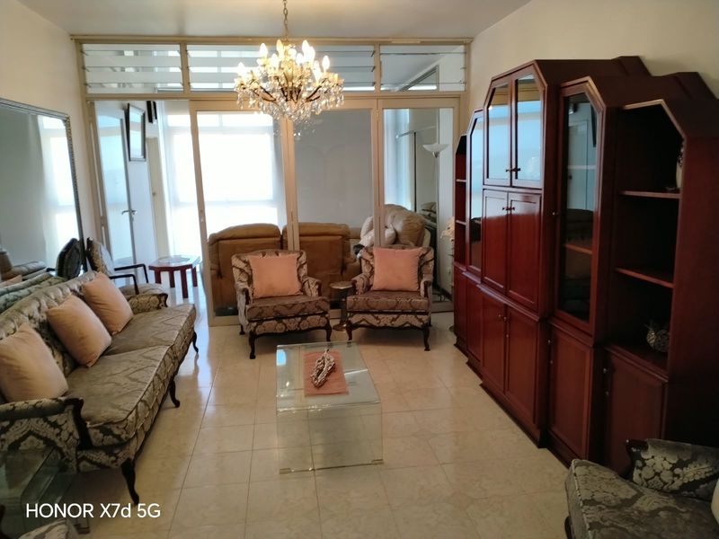 A spacious living room featuring tiled flooring, a crystal chandelier, and large glass sliding doors that provide natural light and access to the exterior.