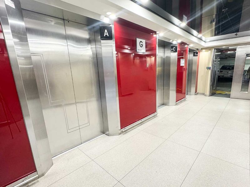 Modern office building elevator lobby featuring polished stainless steel lift doors, high-gloss red wall paneling, and clean tiled flooring.