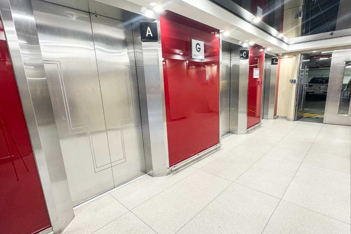 Modern office building elevator lobby featuring polished stainless steel lift doors, high-gloss red wall paneling, and clean tiled flooring.