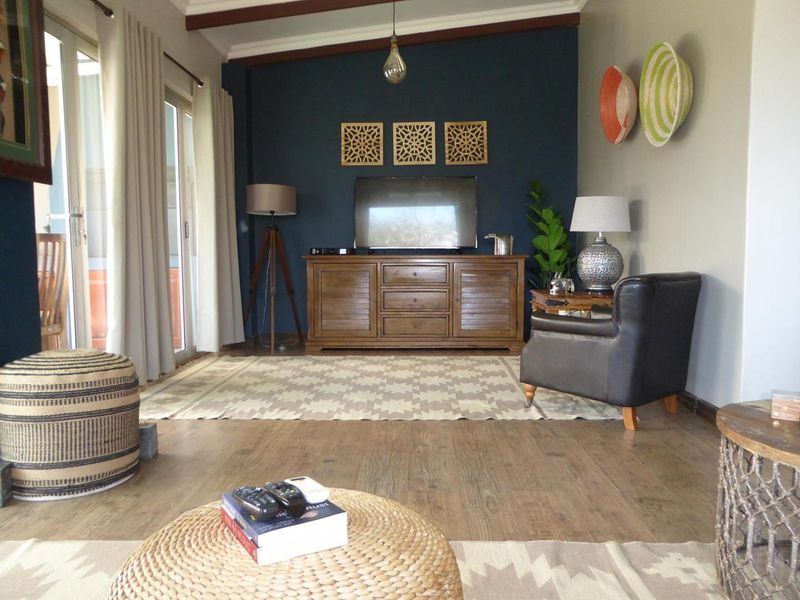 A comfortable living room featuring exposed timber ceiling beams, laminate flooring, and sliding glass doors that provide access to the outdoor area.