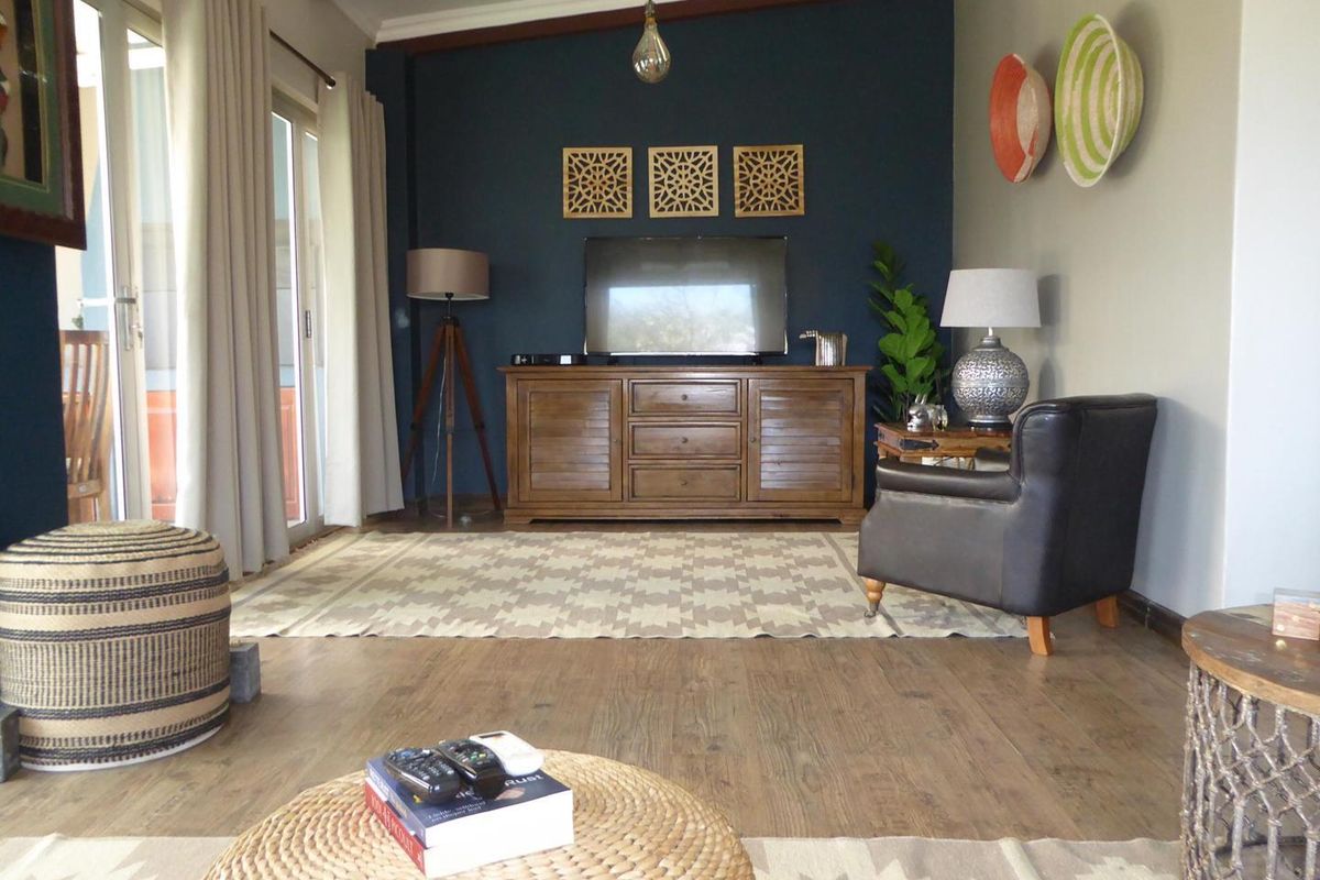 A comfortable living room featuring exposed timber ceiling beams, laminate flooring, and sliding glass doors that provide access to the outdoor area.