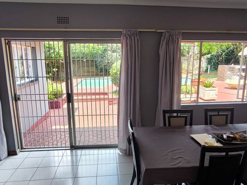 Dining area featuring tiled flooring and large sliding glass doors with security gates, providing direct access to the outdoor patio and pool area.