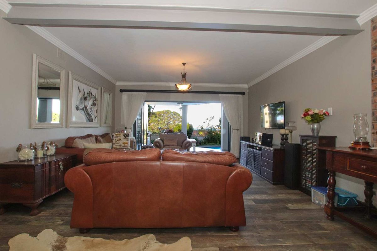 Spacious living room featuring wood-look flooring, crown molding, and large sliding doors that open onto a covered patio and pool area.