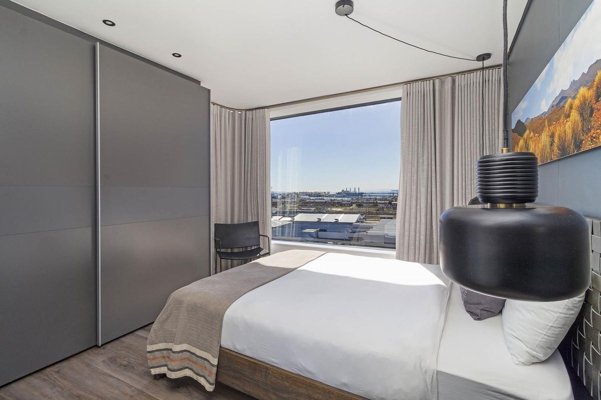 Modern bedroom featuring floor-to-ceiling windows with expansive industrial and coastal views, integrated sliding wardrobe cabinetry, and contemporary recessed lighting.