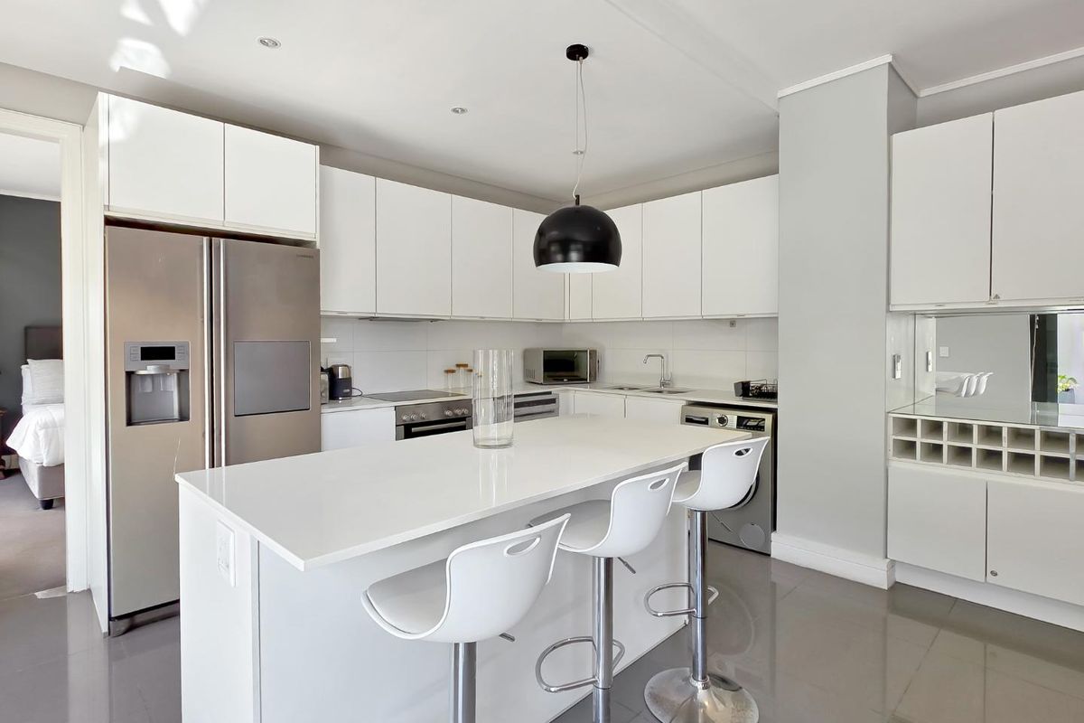 Modern kitchen featuring white cabinetry, a central island with quartz countertops, stainless steel appliances, and integrated wine storage, finished with sleek tiled flooring.