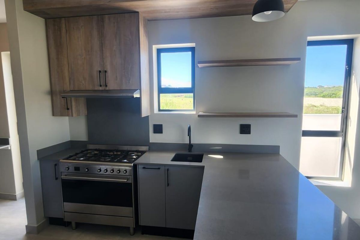 Modern kitchen featuring sleek grey cabinetry, stone countertops, a built-in gas stove with extractor fan, and open shelving, offering a clean and contemporary aesthetic.