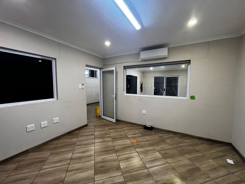 A clean, empty office space featuring tiled flooring, split-system air conditioning, and ample natural light through aluminium-framed windows.