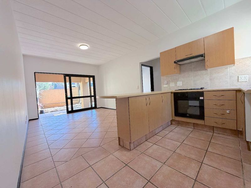 Open-plan kitchen and living area featuring tiled floors, built-in cabinetry with integrated oven and hob, and a sliding door leading to an outdoor space.