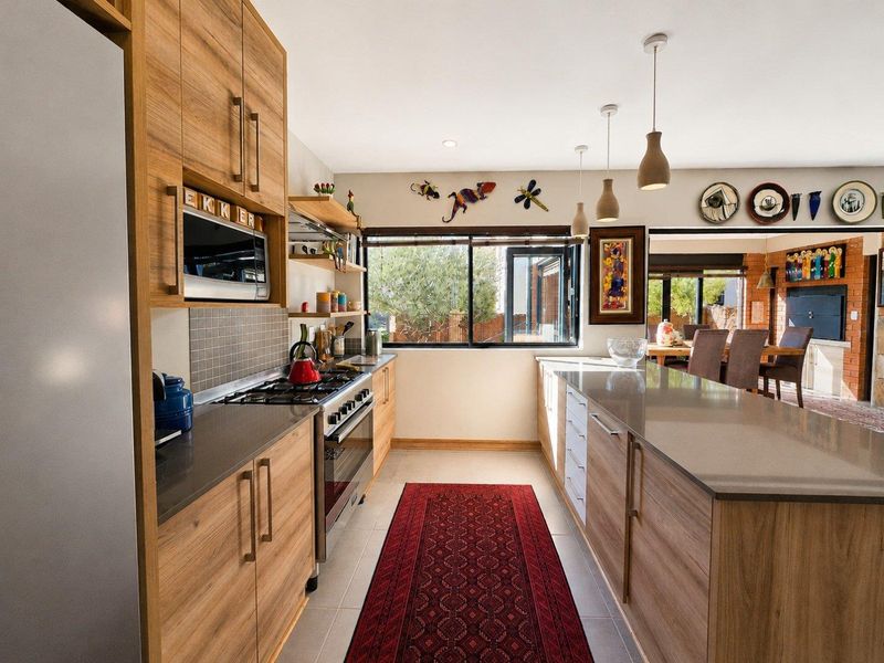 Modern kitchen featuring wood-finish cabinetry, stone countertops, a central island, and integrated appliances, flowing into an open-plan dining area.