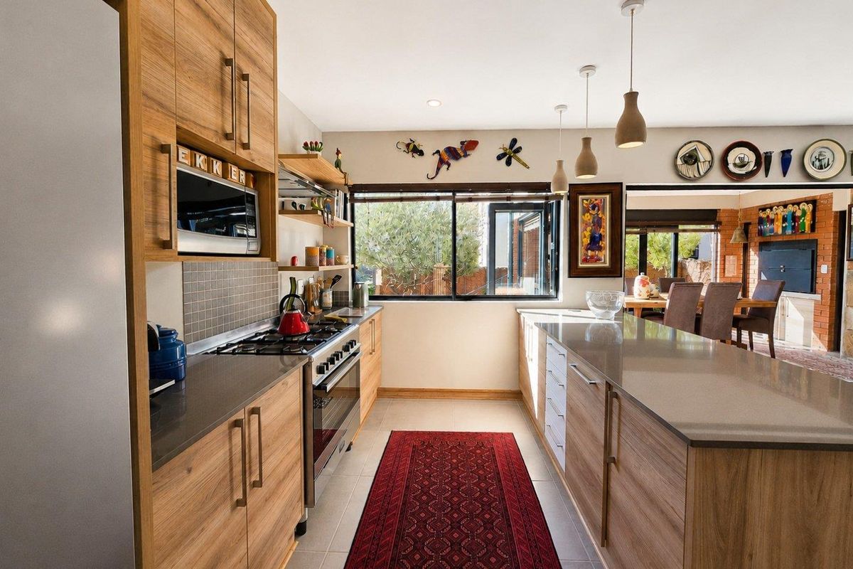 Modern kitchen featuring wood-finish cabinetry, stone countertops, a central island, and integrated appliances, flowing into an open-plan dining area.