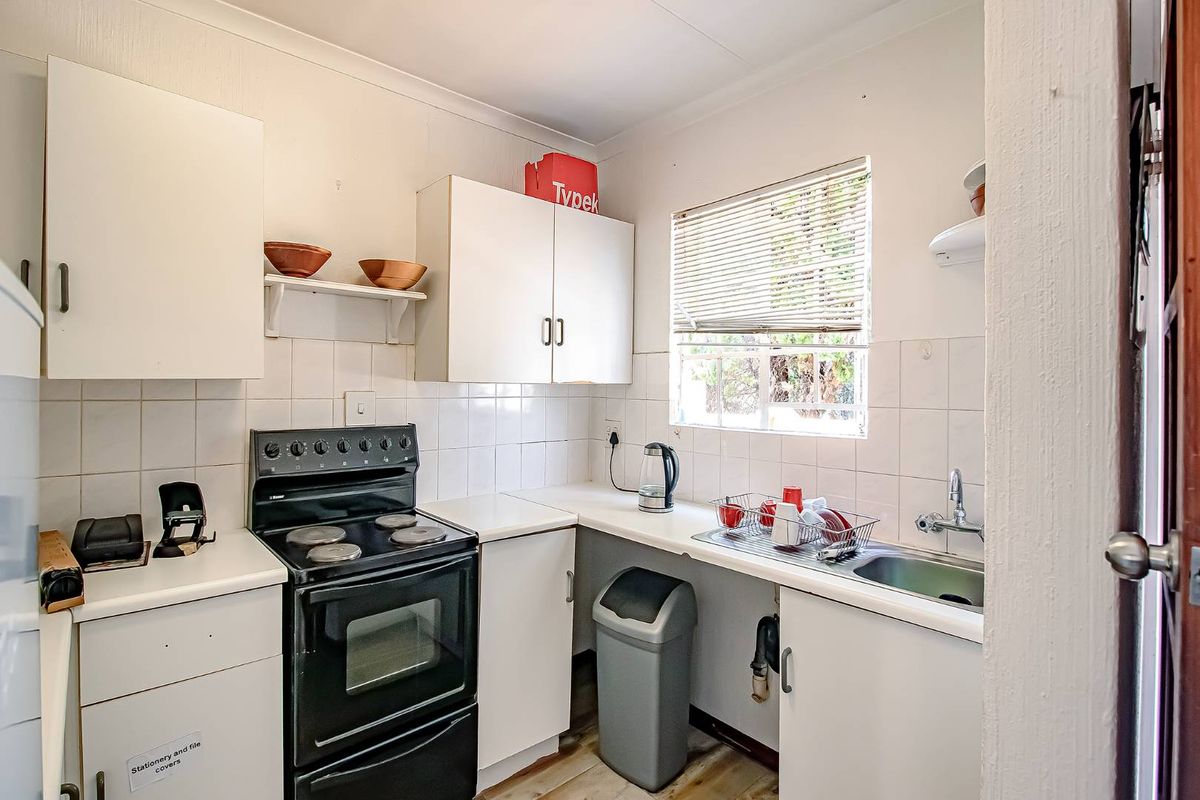 A compact kitchen featuring white cabinetry, a built-in stove, a stainless steel sink, and tiled splashbacks, offering a functional layout for daily meal preparation.