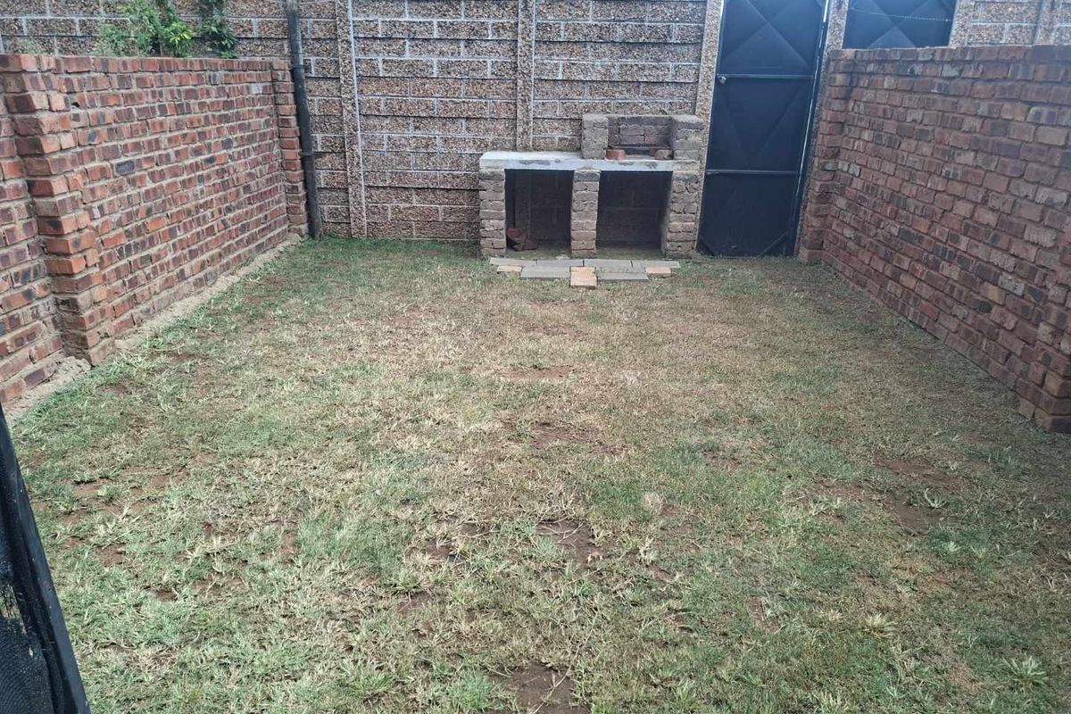 A private rear courtyard featuring a built-in brick braai area, enclosed by high perimeter brick walls and a secure metal gate.