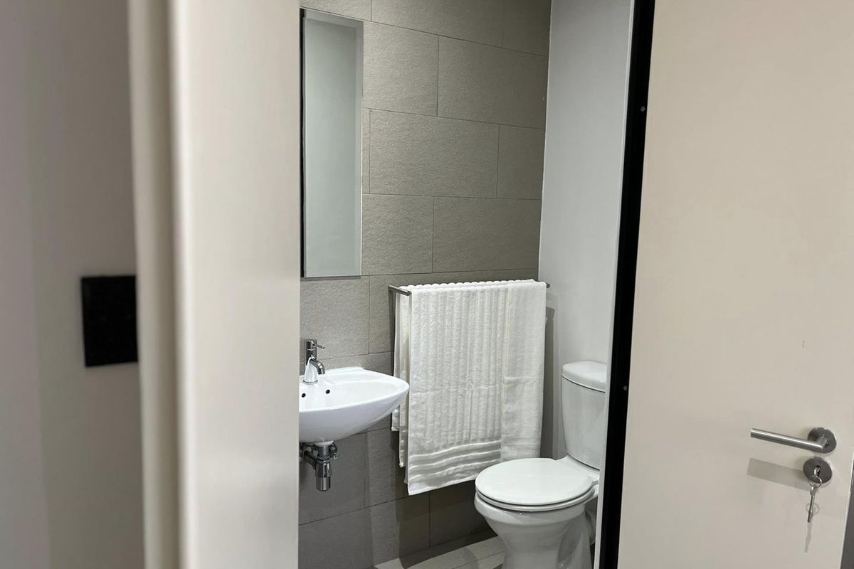 A compact, modern bathroom featuring a wall-mounted basin, toilet, and neutral-toned tiled walls and flooring.