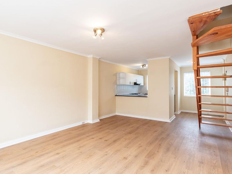 Open-plan living area featuring laminate flooring, a wooden staircase, and a compact kitchen with built-in cabinetry and a breakfast counter.