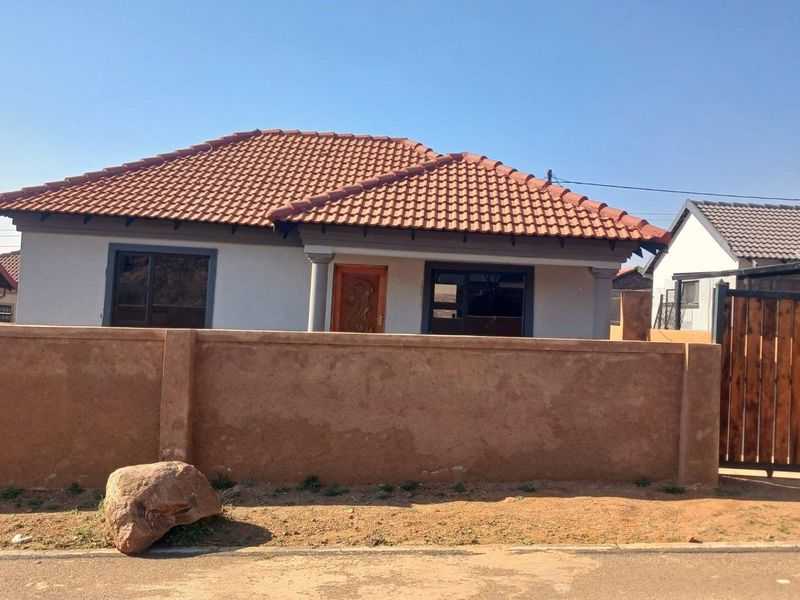 Front view of a single-story house featuring a tiled roof, aluminium window frames, and a perimeter boundary wall with a wooden gate.