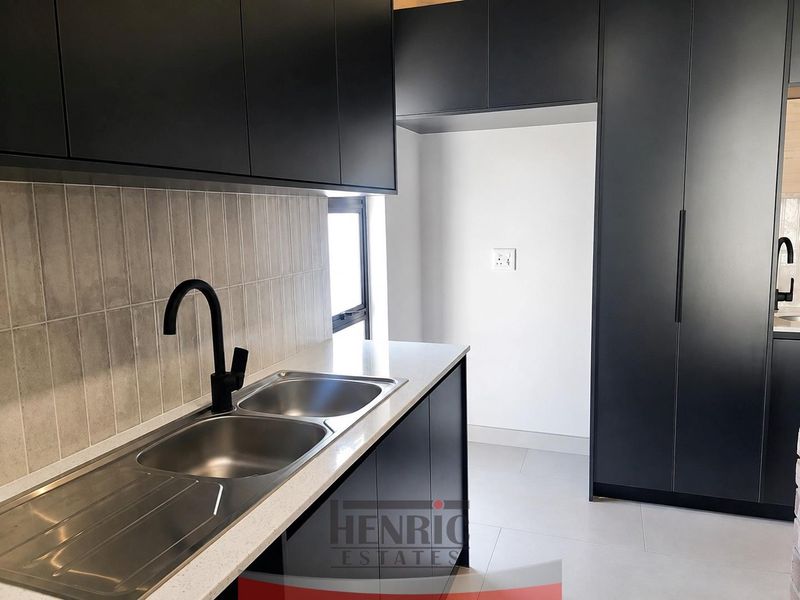 Modern kitchen featuring sleek matte black cabinetry, stone-look countertops, a double stainless steel sink with a black mixer tap, and contemporary tiled backsplash.