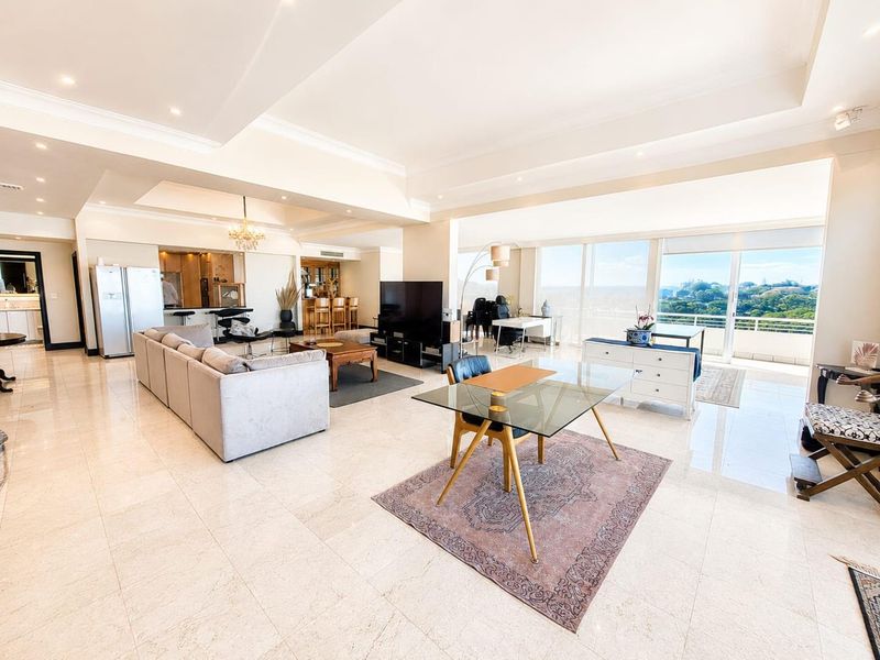Spacious open-plan living and dining area featuring polished marble flooring, recessed ceiling lighting, and expansive sliding glass doors leading to a balcony with scenic views.
