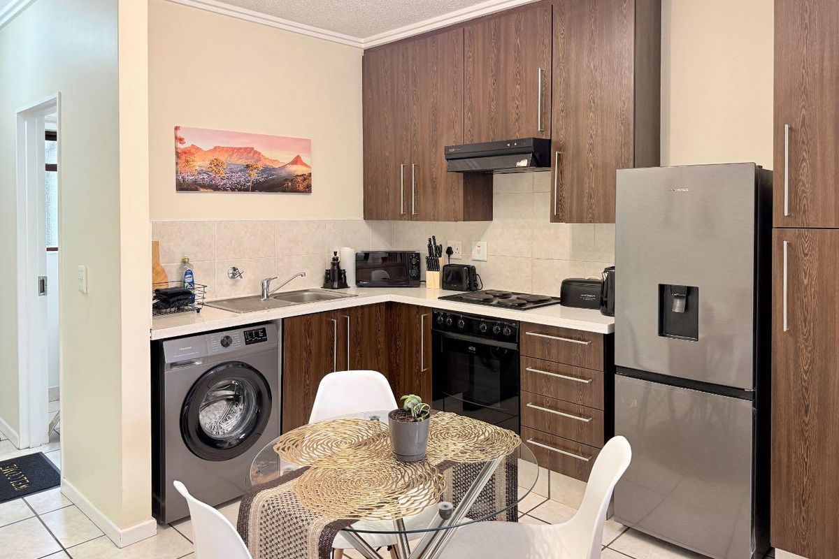 Compact kitchen featuring dark wood cabinetry, tiled backsplash, built-in oven with hob, extractor fan, and space for a washing machine.