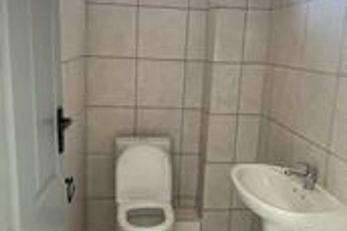 A compact office restroom featuring a pedestal sink, a standard toilet, and full-height wall tiling.