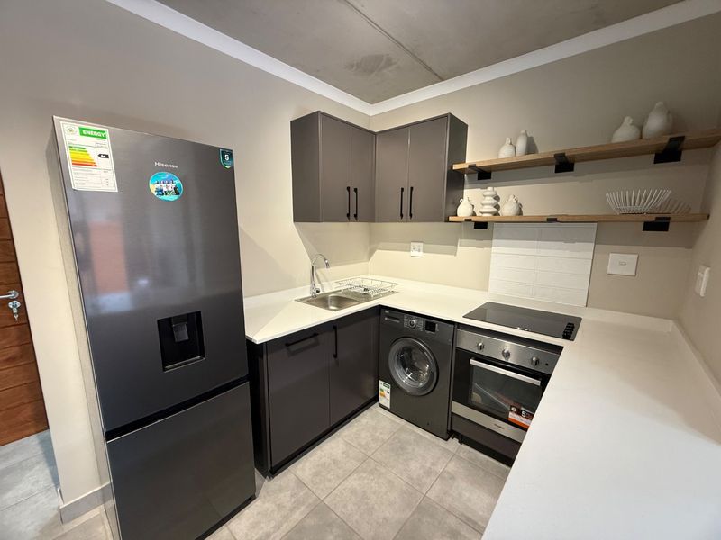 Modern kitchen featuring dark cabinetry, quartz countertops, integrated oven, electric hob, and tiled flooring in a clean, contemporary design.