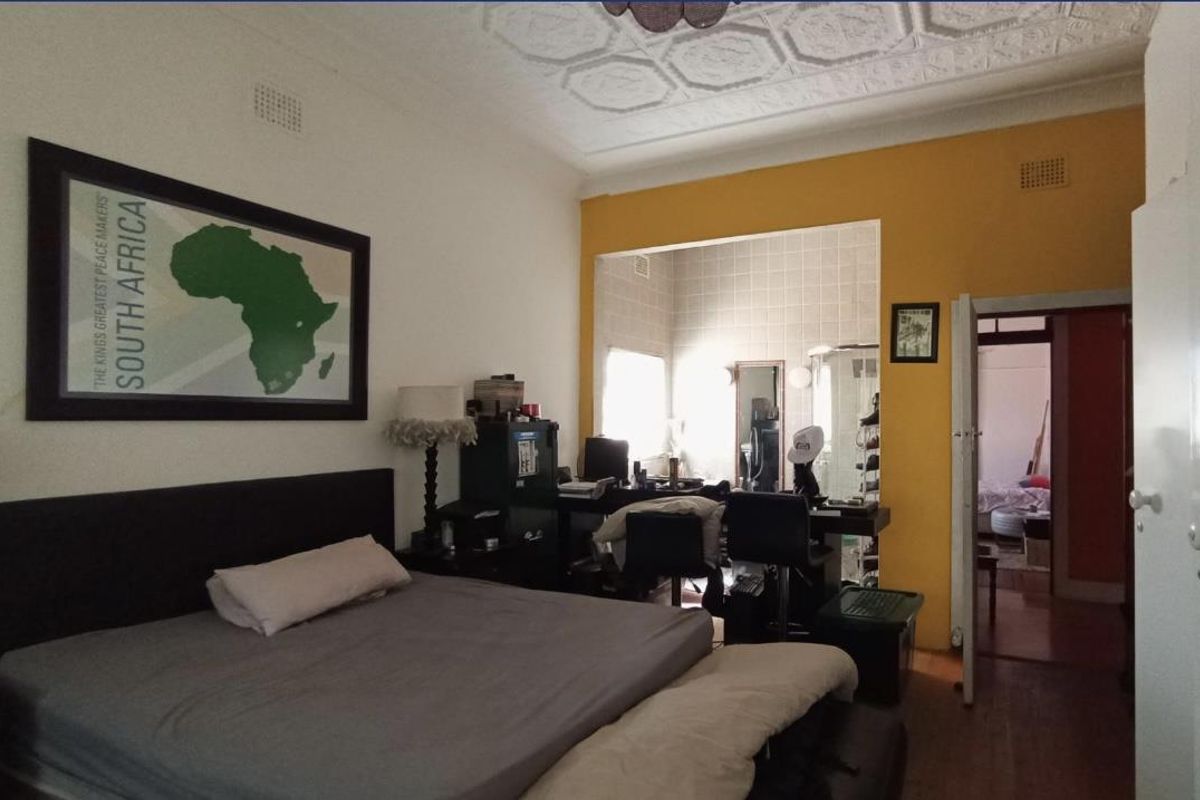 Spacious bedroom featuring high ceilings with decorative plasterwork, hardwood flooring, and an adjoining dressing or study area.