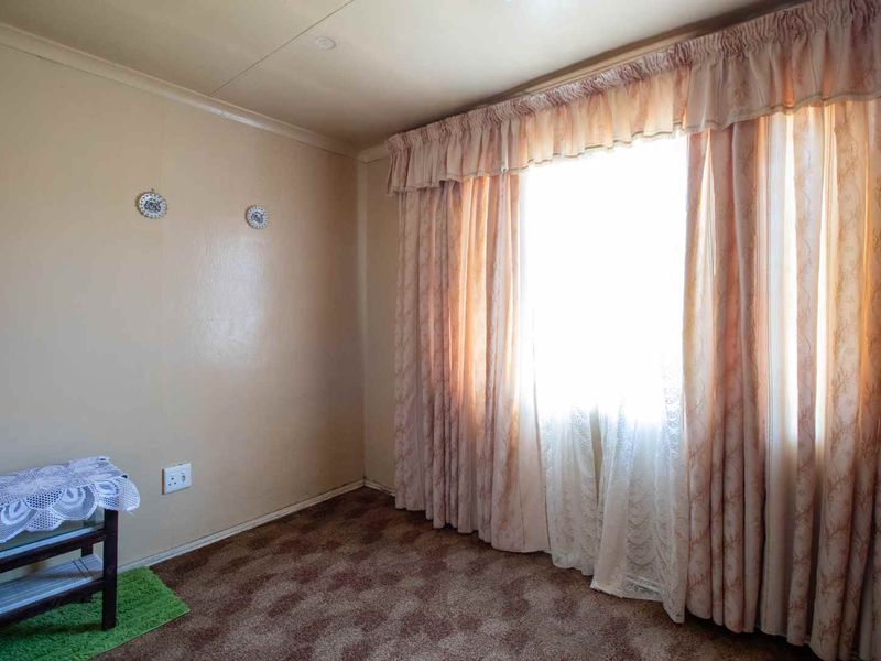 A vacant bedroom featuring carpet flooring and large windows with curtain rails, offering a blank canvas for renovation and modernization.