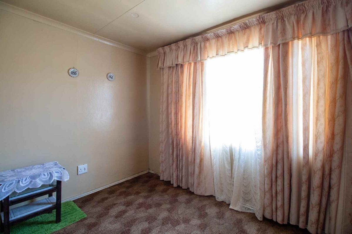 A vacant bedroom featuring carpet flooring and large windows with curtain rails, offering a blank canvas for renovation and modernization.