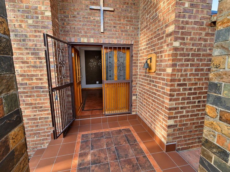A welcoming front entrance featuring a face brick facade, stone cladding accents, a secure metal gate, and a solid wooden front door.