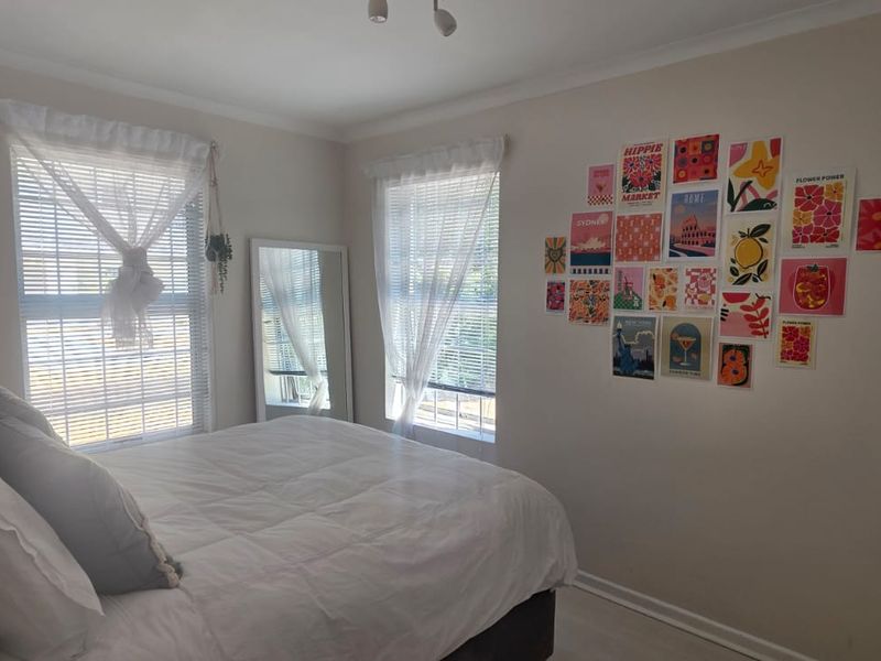A bright bedroom featuring neutral walls, built-in wardrobe storage, and dual windows with venetian blinds, offering a clean and functional living space.