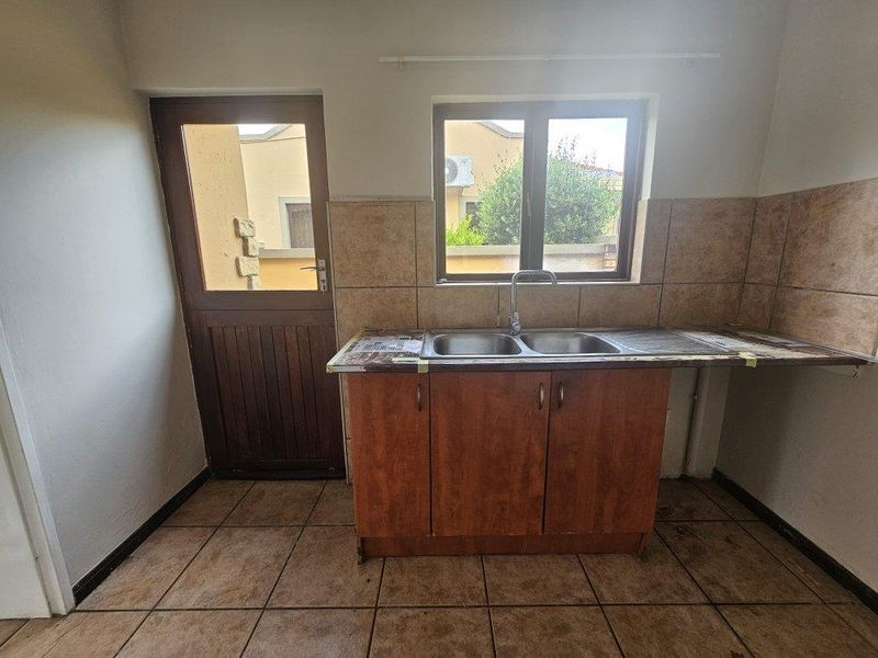 A functional scullery area featuring a double basin sink, laminate countertop, base cabinetry, and direct access to the exterior.