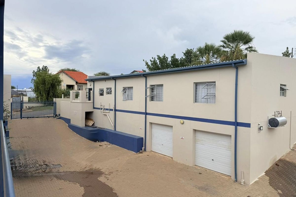 Exterior view of the apartment building featuring a paved driveway, two garage doors, and external wall-mounted geyser unit.