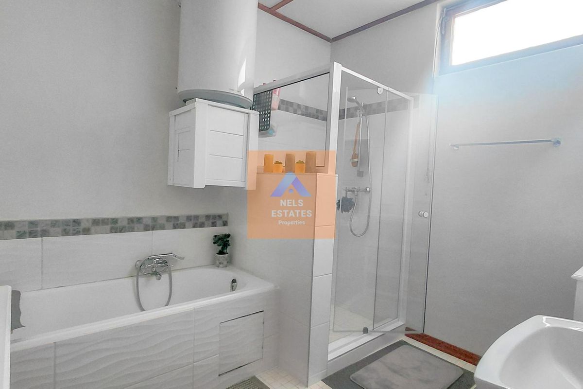 A functional bathroom featuring a bathtub, separate shower enclosure, wall-mounted water heater, and tiled splashback finishes.