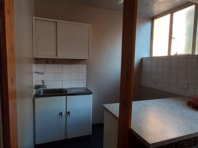 A compact, dated kitchen area featuring built-in cabinetry, a sink with tiled splashback, and a functional countertop space.
